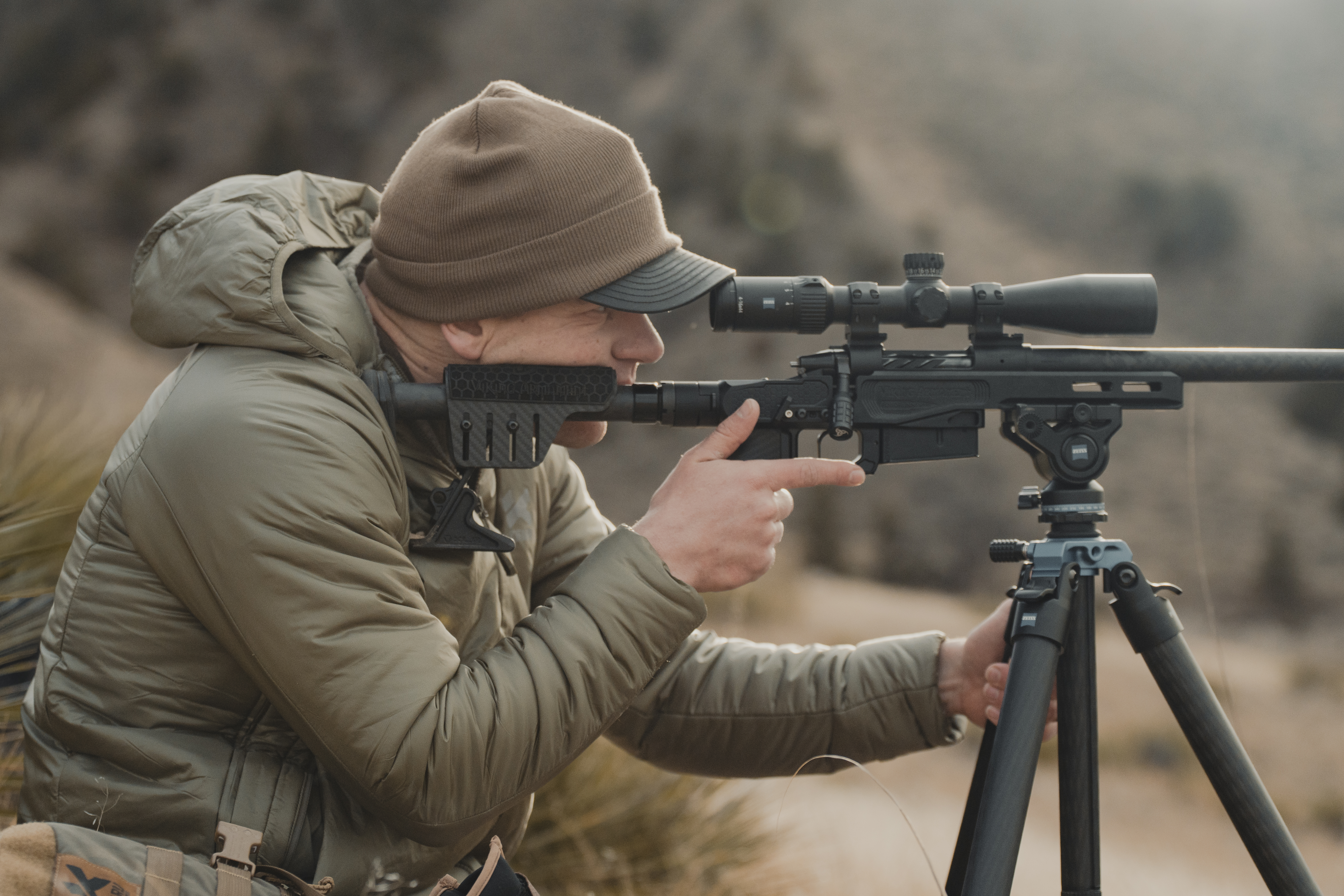 A hunter taking aim with a rifle on a tripod.