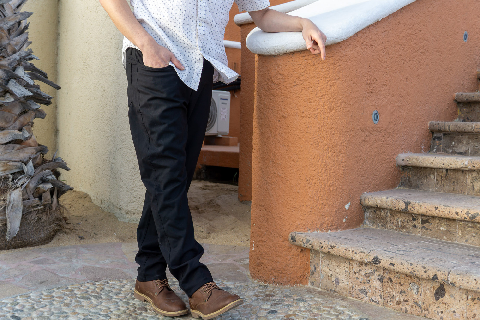 the author poses in the unbound merino travel pants beside a stone staircase in cabo san lucas, mexico