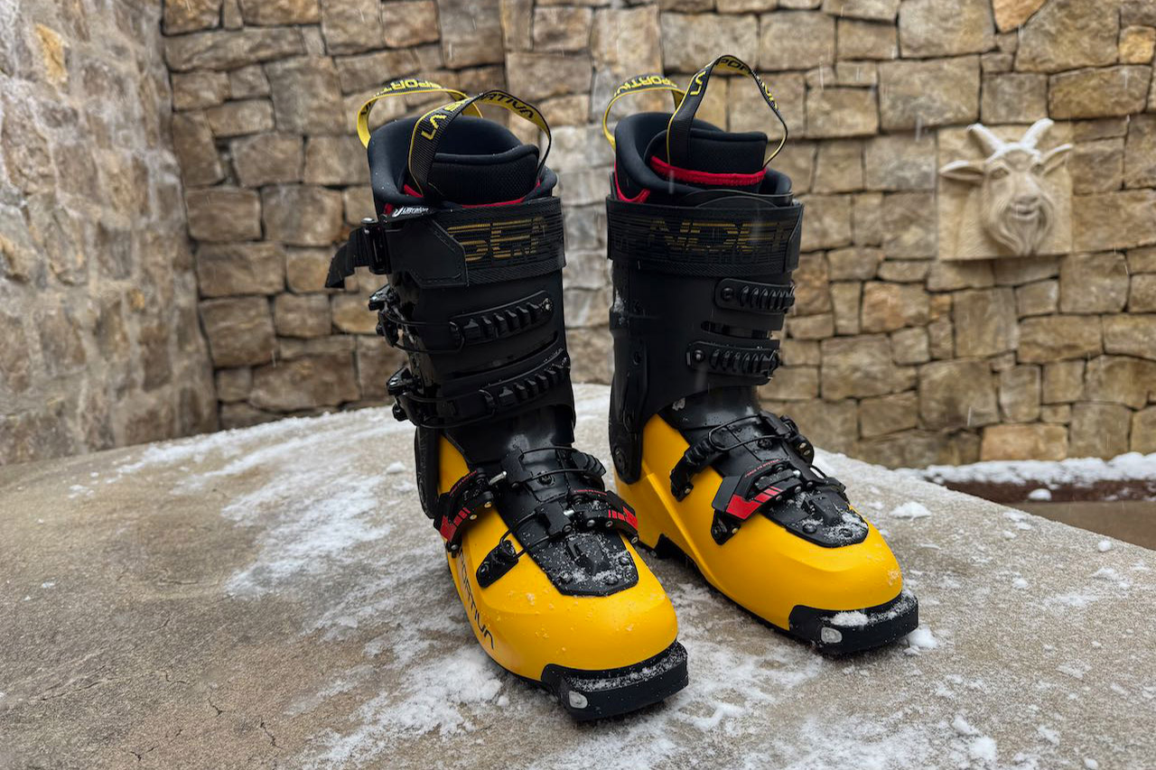 A pair of La Sportiva Sender ski boots stands upright side by side on a snowy stone platform