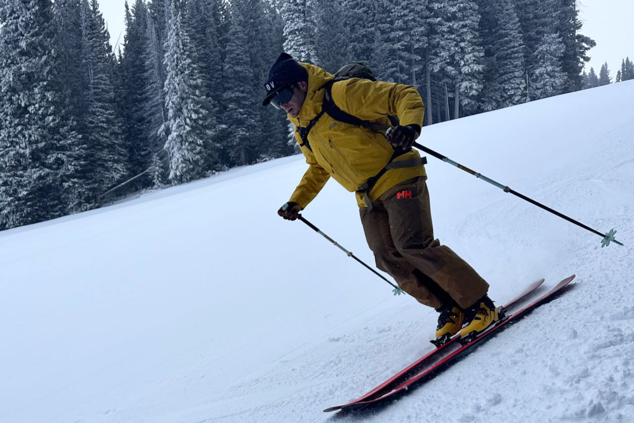 The Sender boots are worn while skiing downhill on a groomed run with trees in the background