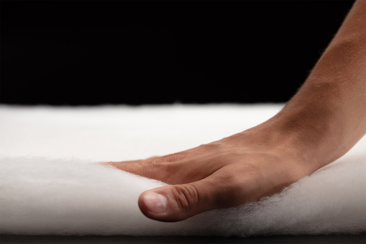 A hand presses down on white PrimaLoft insulation, showing the material compressing against a flat surface