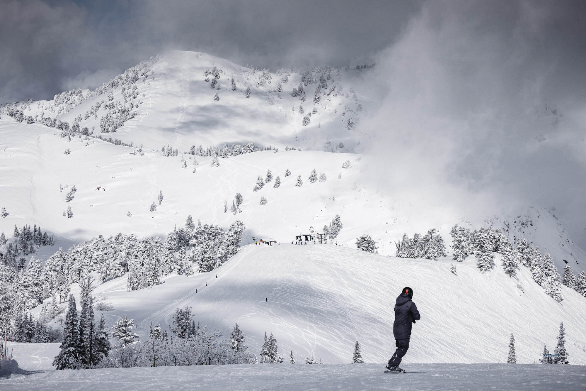 A snowboarder carves down a slope at Powder Mountain, with misty peaks in the background