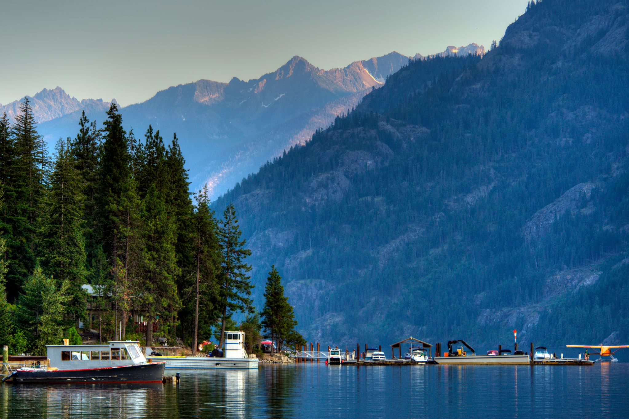 Multiple boats on a lake with trees on the left and mountains in the background