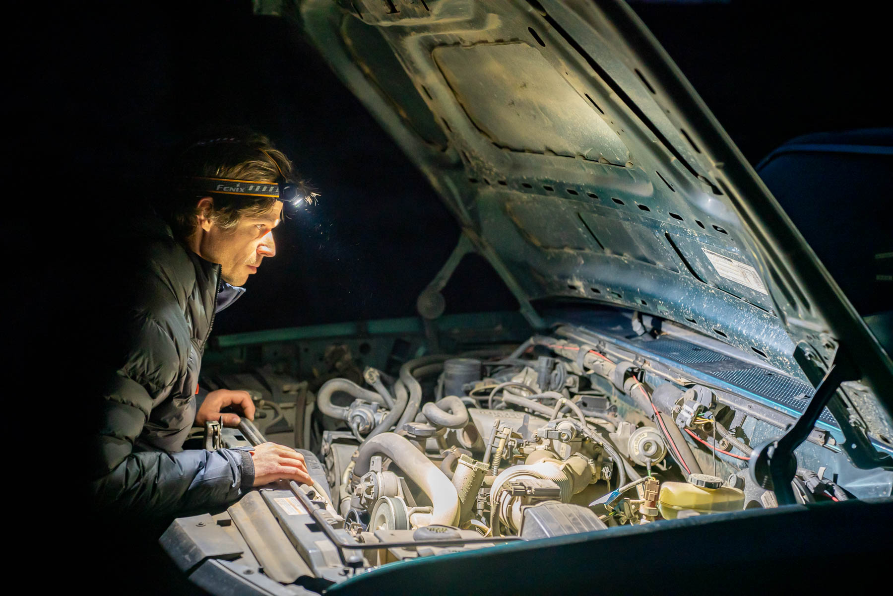 Man looking under truck hood while wearing headlamp