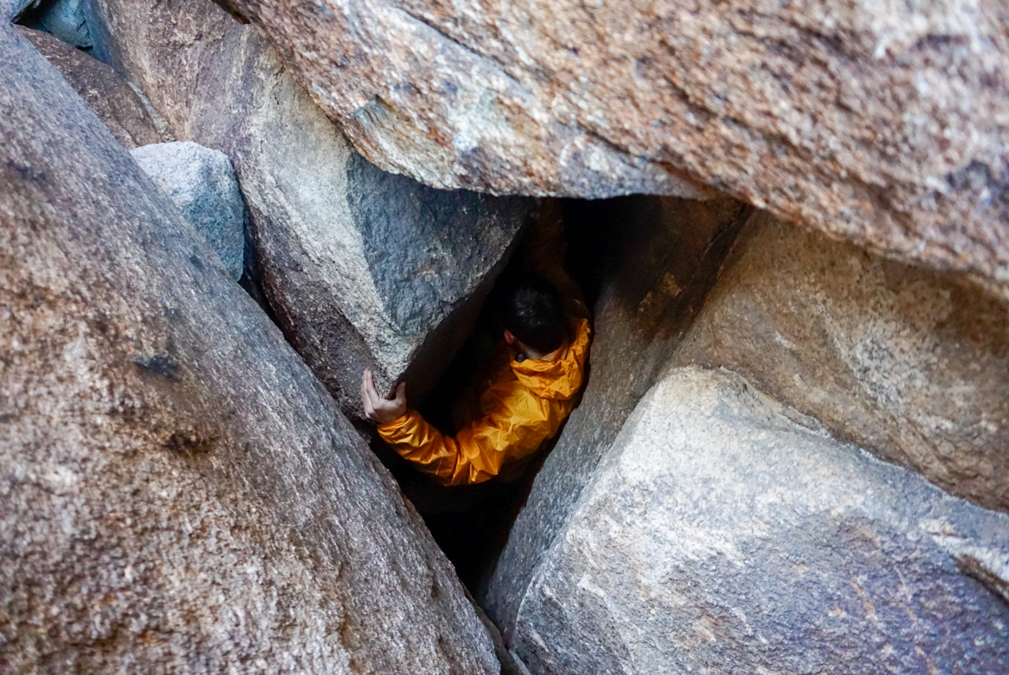 A Climber Descends Into a Hole in the Rock Wearing the Outdoor Research Helium Rain Jacket