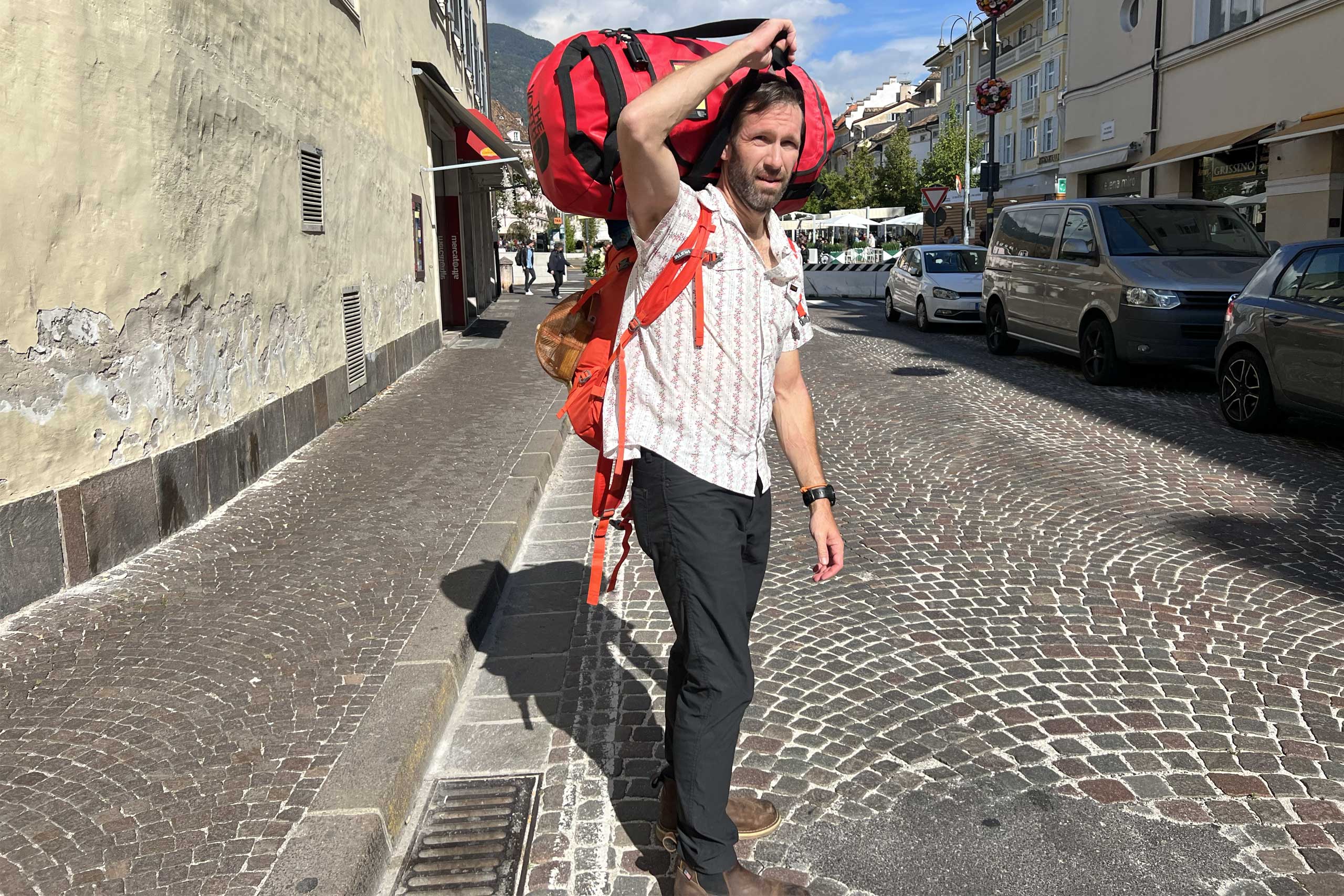 A man on a coblestone streat with a suitcase