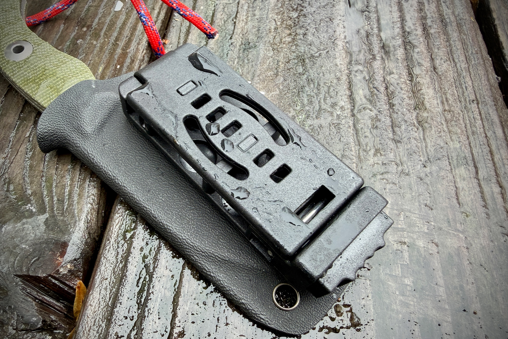 The Kizer Rook in its sheath with the belt clip closed on a wet wooden surface