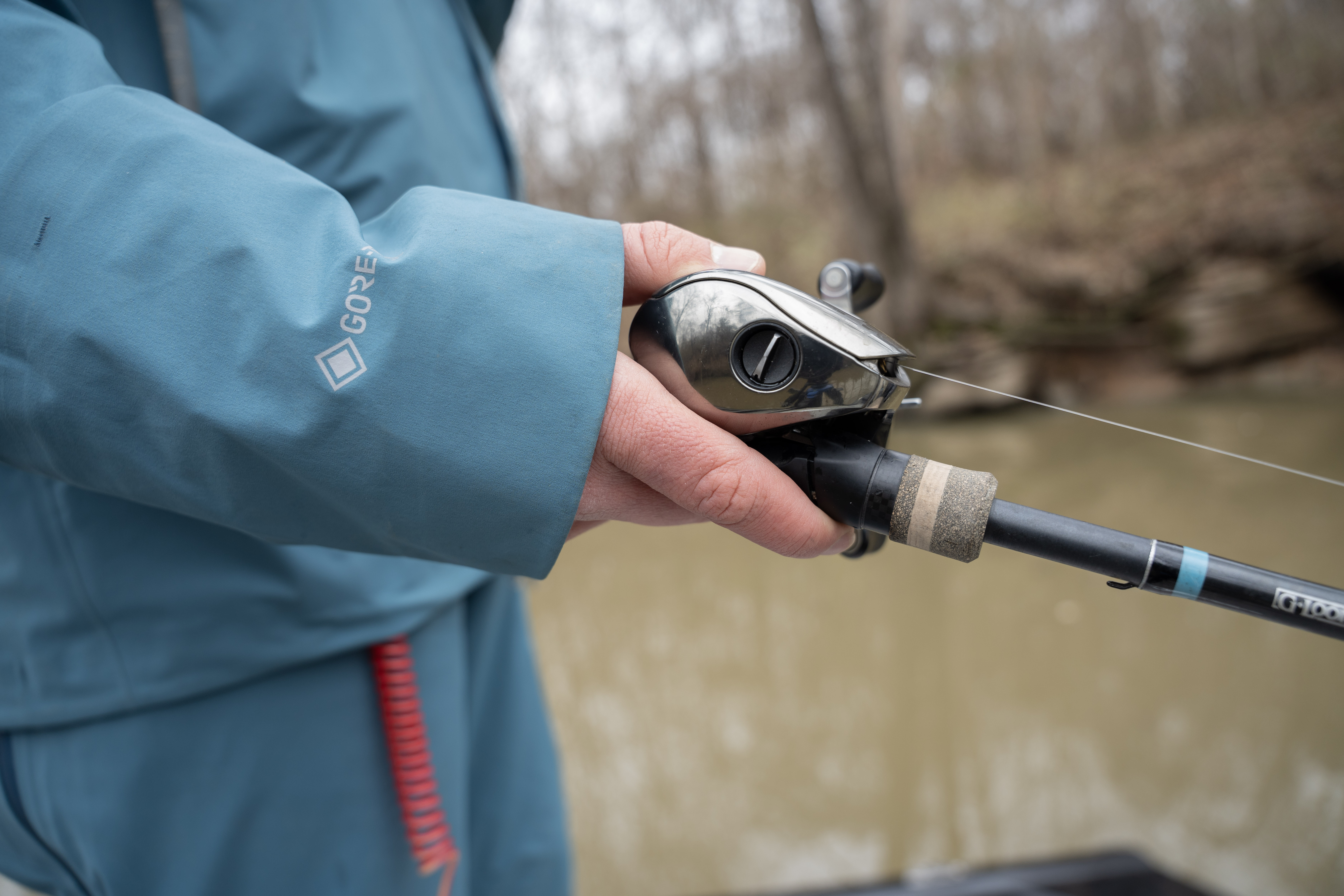 A close shot of a hand holding a fishing rod and bait caster.