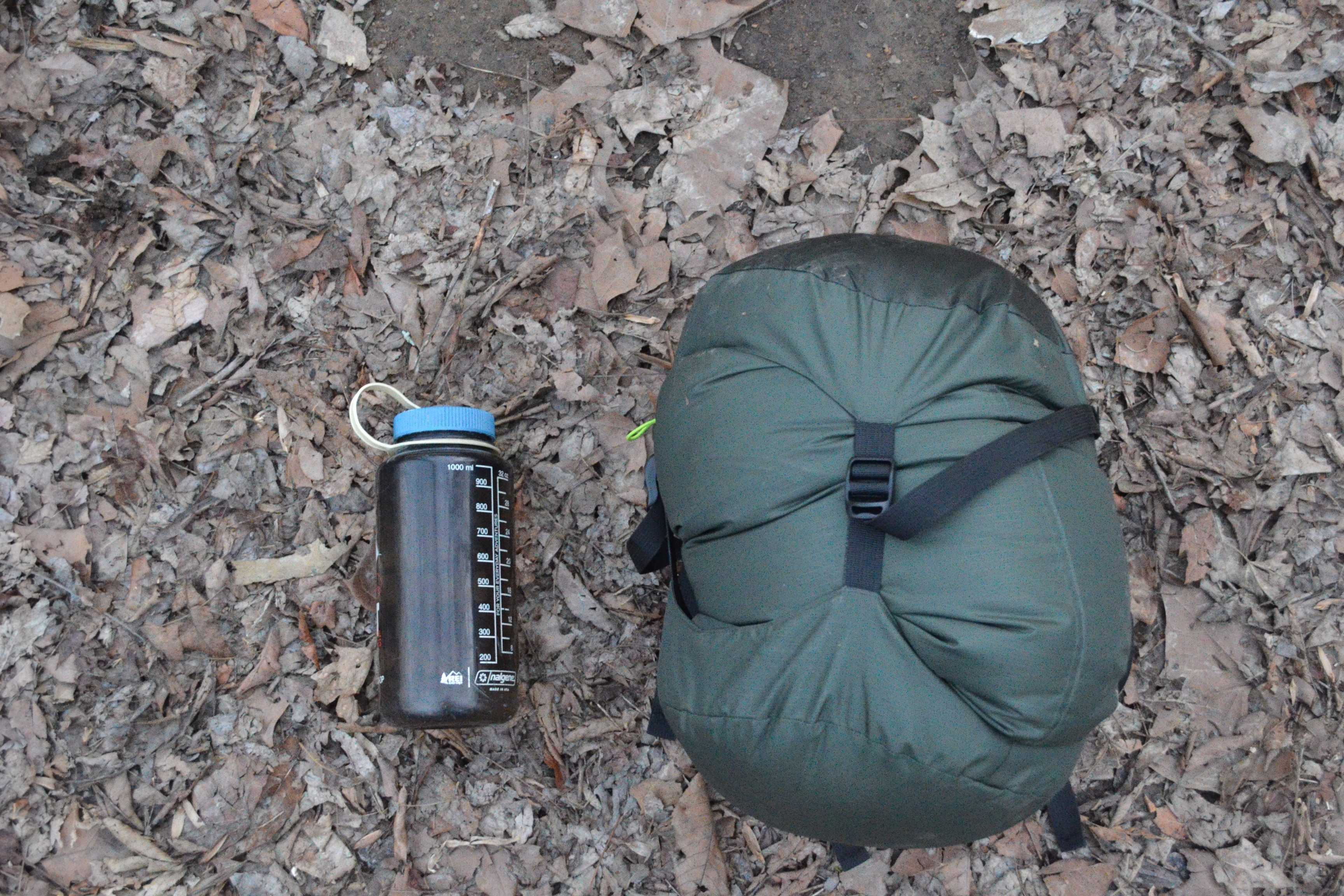 sleeping bag in stuff sack next to water bottle on ground