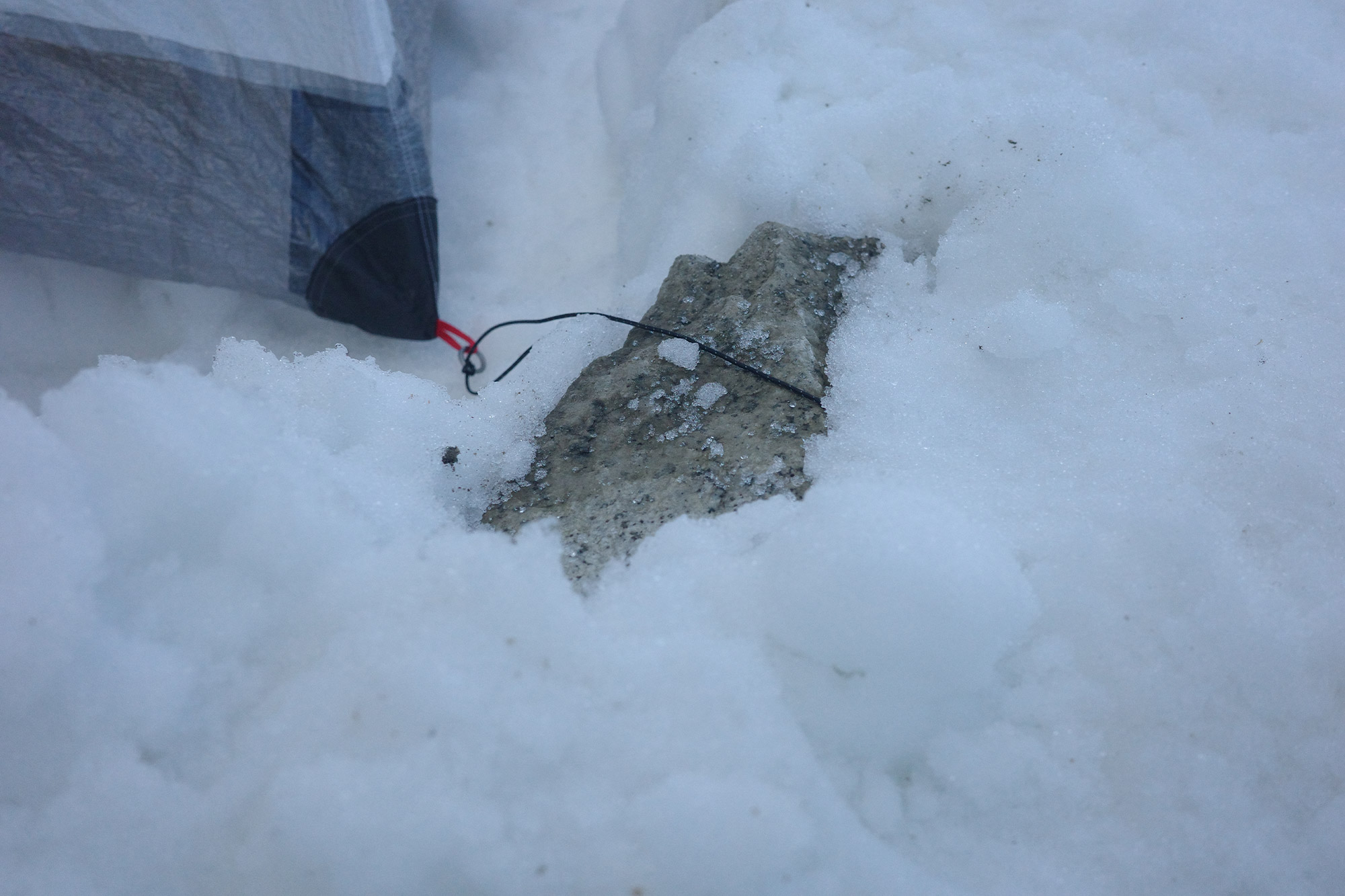 Tent anchored in snow using a rock and cord system