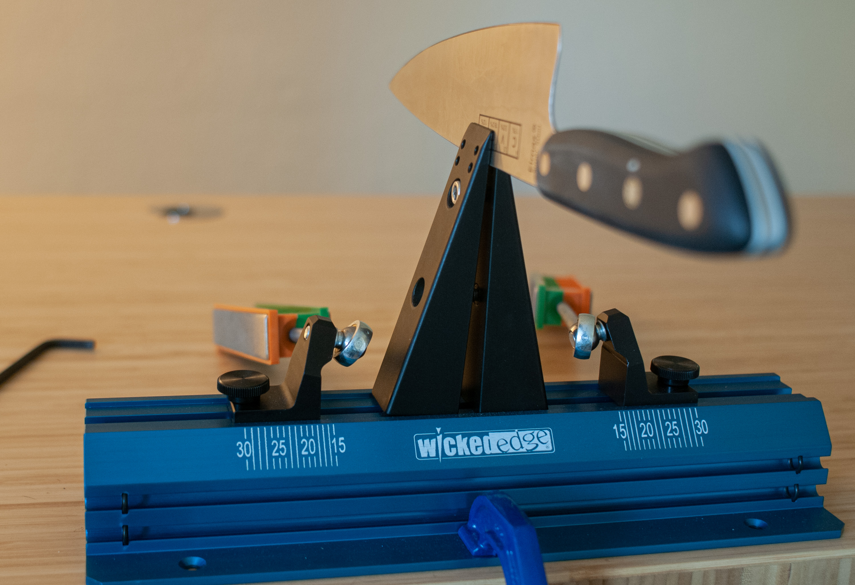 a smaller knife clamped in the jaws of a wicked edge knife sharpener on a desk