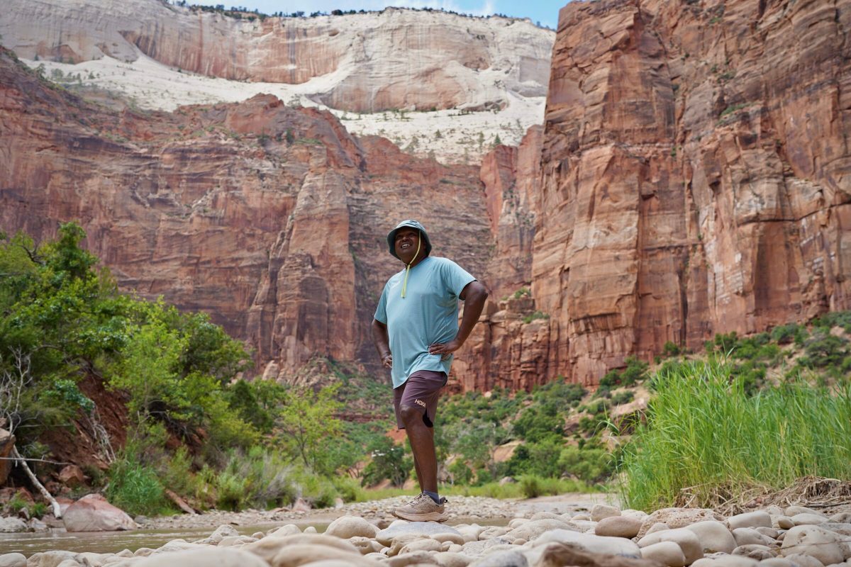 A man stands next to a river while wearing hiking shoes