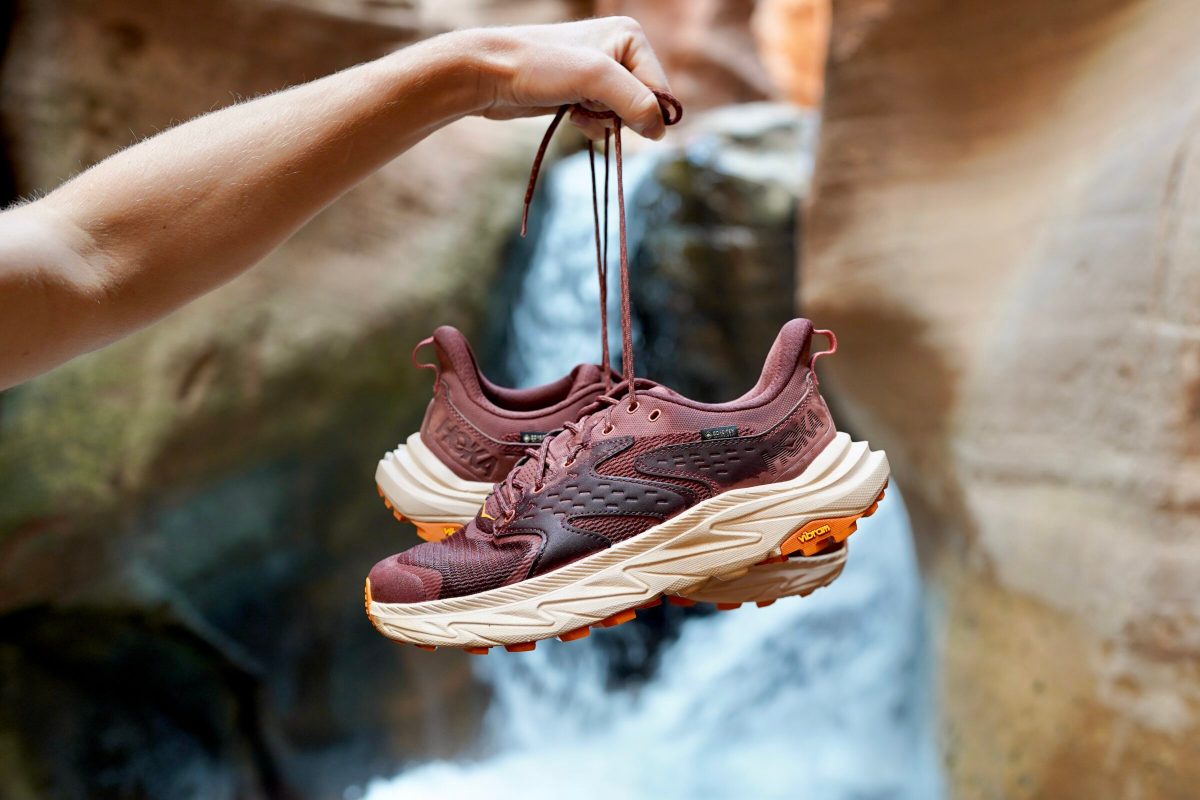 A woman holds up a pair of hiking shoes in front of a waterfall