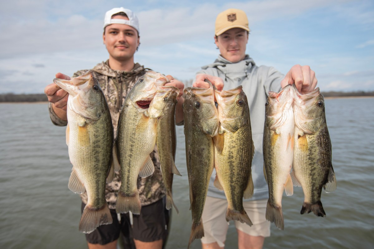 Two young men holding bass in front of a lake.