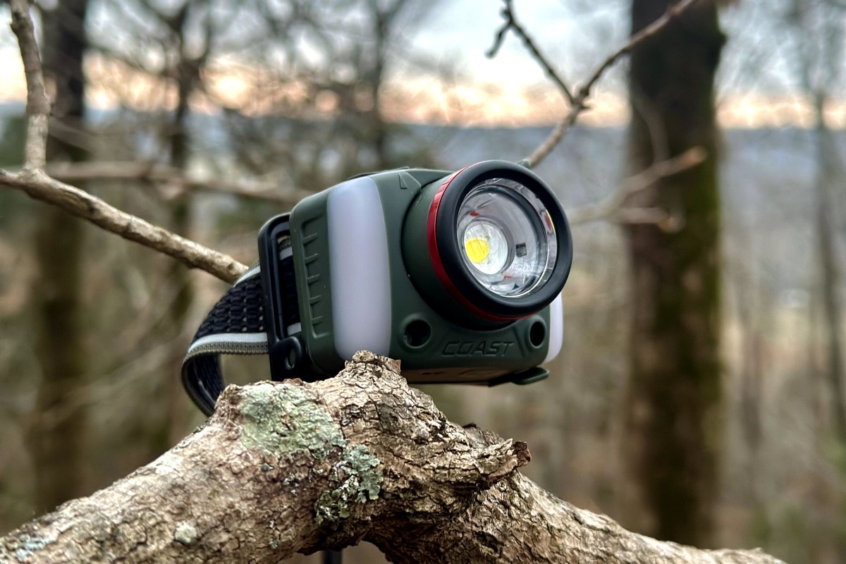 The sun setting behind a hill behind the Coast FL97R headlamp resting on a branch.