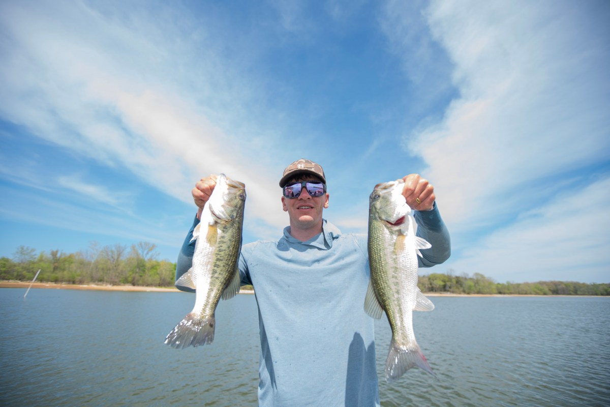 An angler wearing the Bajio Cocho sunglasses while holding two bass on a bright day.