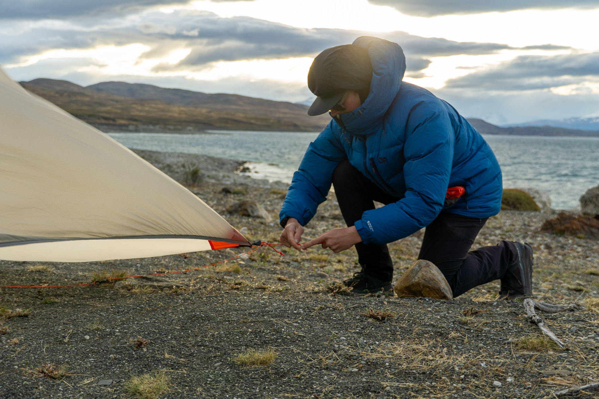 the author sets up a tarp shelter in patagonia while wearing a blue parka