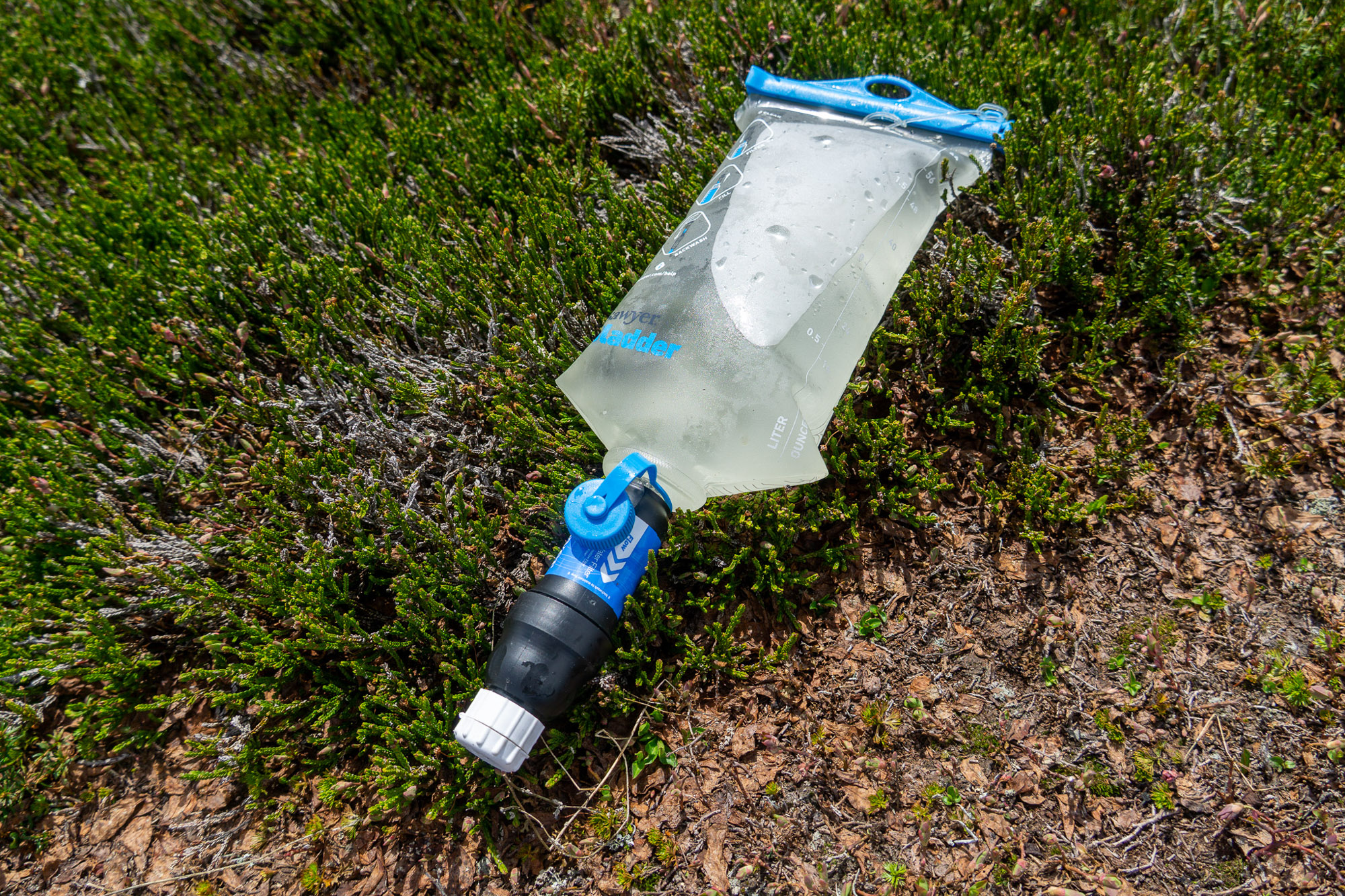 the sawyer squeeze filter and cnoc filter bag connected and filled with water on a bed of alpine heather in washington state