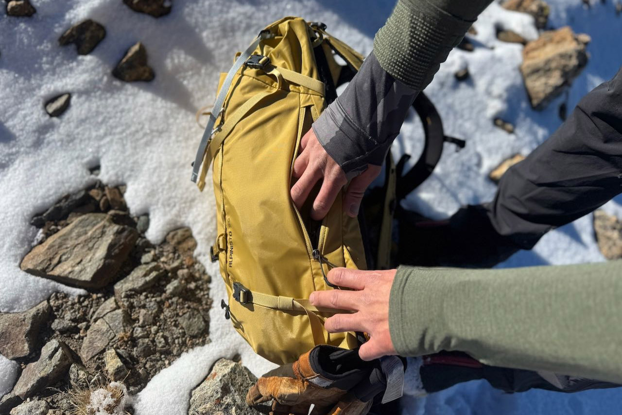 Side zipper pocket on the Gregory Alpinisto 30 pack being opened on snowy terrain