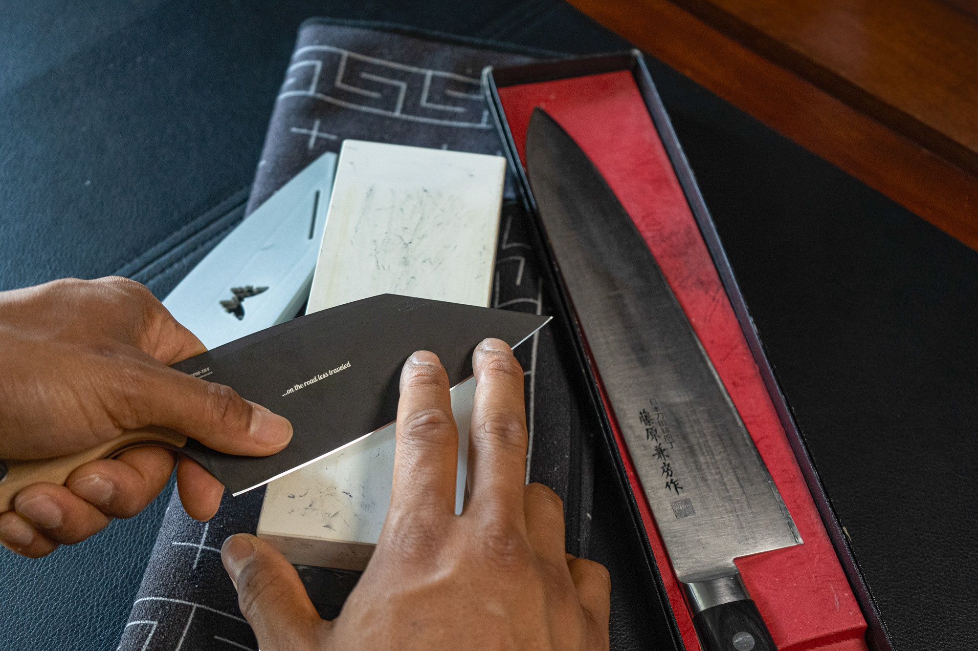 a set of hands pass a large knife across a ceramic whetstone, guiding the angle as it passes