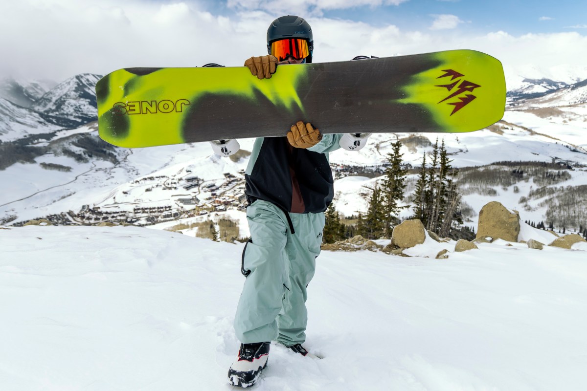 Rider holds the Jones Howler snowboard horizontally showing the base graphic