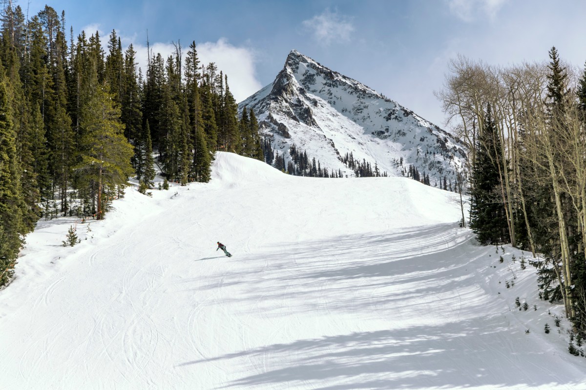 Snowboarder rides the Jones Howler on a wide open run with mountain backdrop