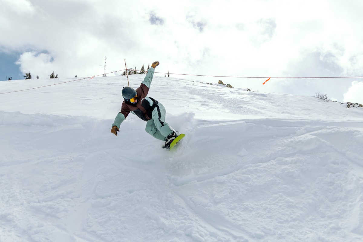 Rider carves through soft snow with the Jones Howler snowboard on a steep slope
