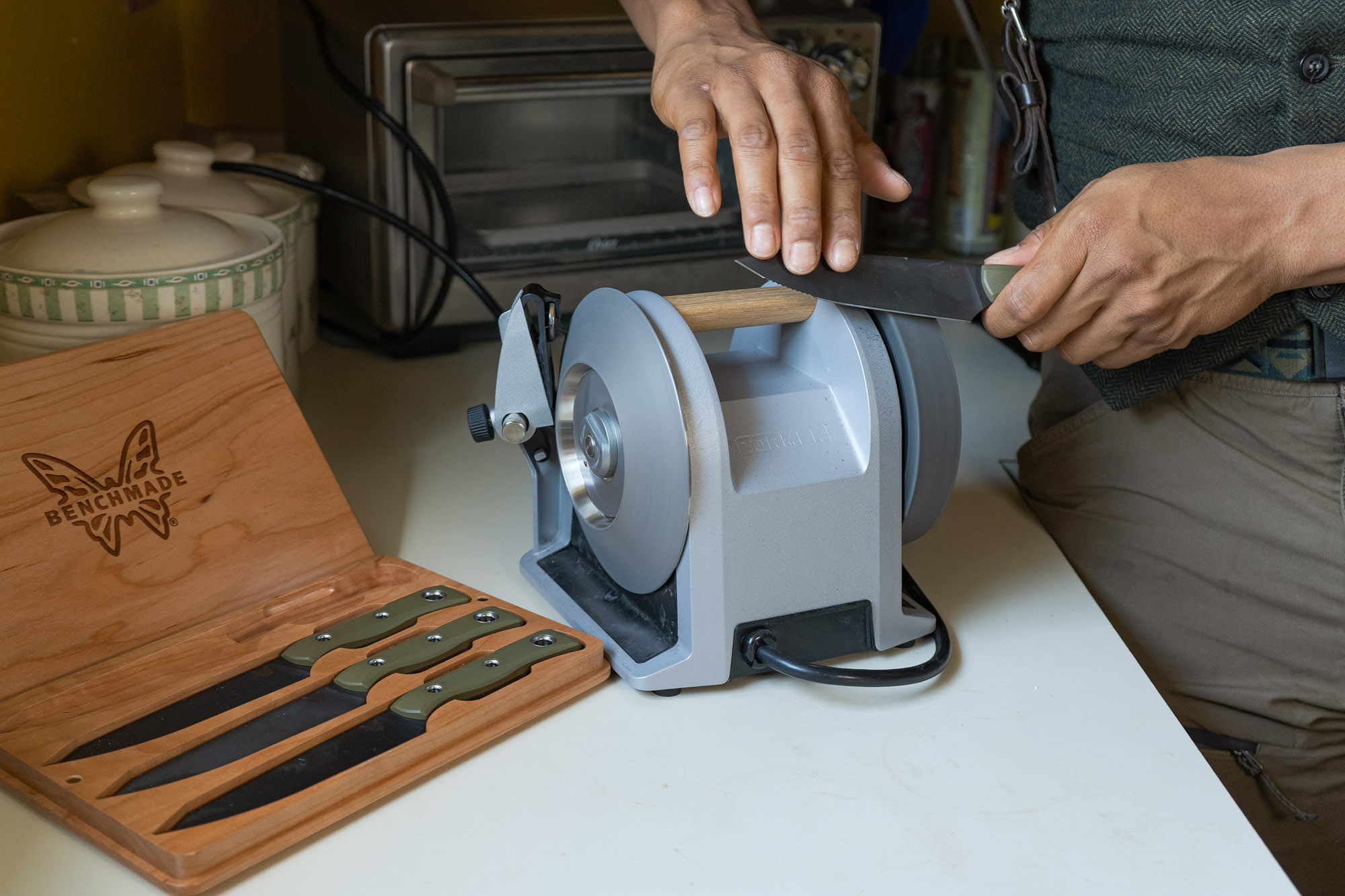 a tormek electric sharpener on a kitchen countertop, with the author sharpening a benchmade kitchen knife on it