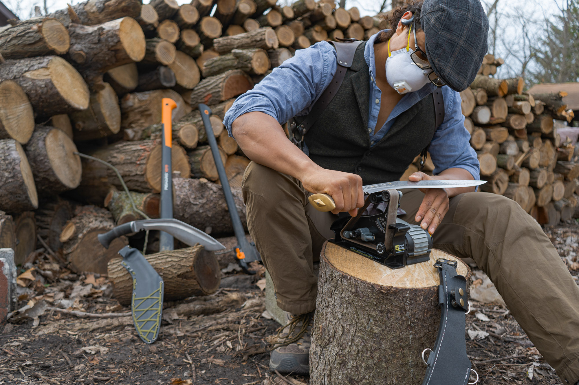the author wears a mask as he sharpens a khukuri on a work sharp mk.2 sharpener in a wood yard
