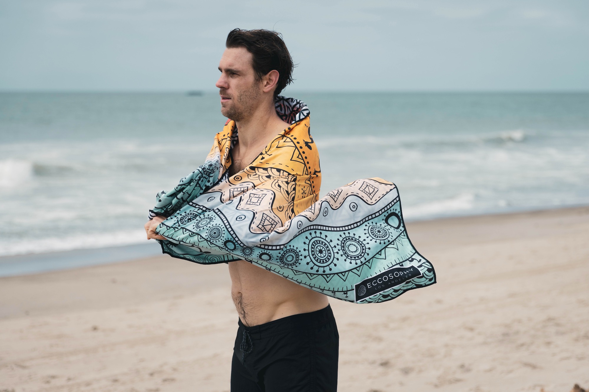 A man wrapped in the Eccosophy Microfiber beach towel after getting out of the ocean