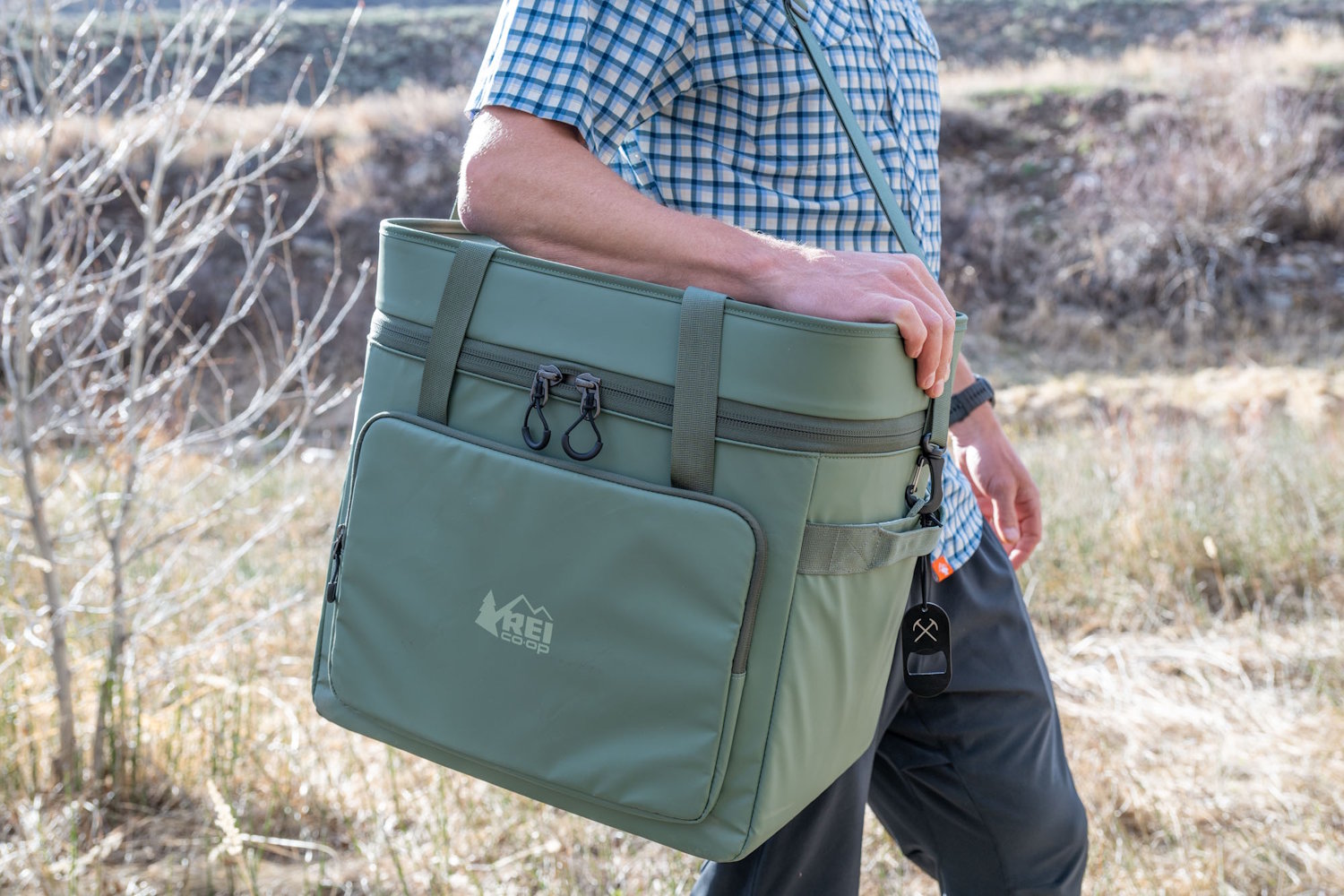 A man carrying the large green REI Trail Gate cooler over his shoulder using the adjustable padded strap.