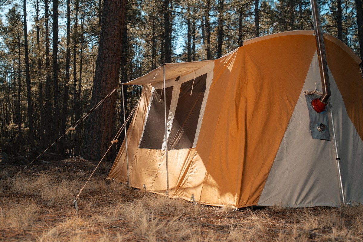 Skyliner hot tent rear wall with mesh windows, guy lines, and a stove pipe in a wooded campsite