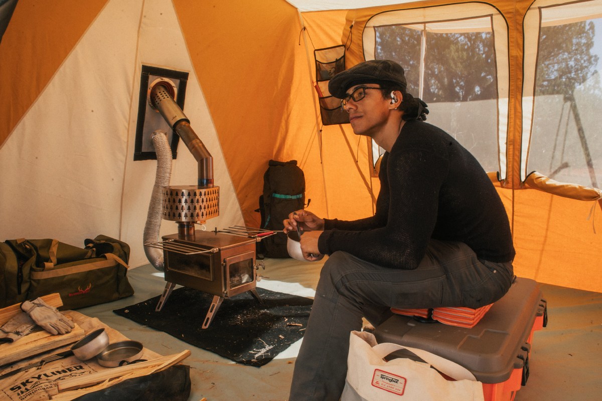 A person sits beside the wood stove inside the Skyliner hot tent