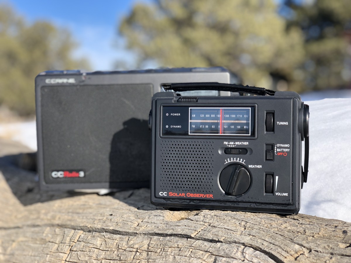 two c.crane emergency radios sit on a log before a snowy background