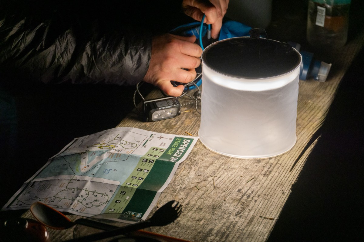 a camper uses the light of the biolite luci charge 360 to read a map beside