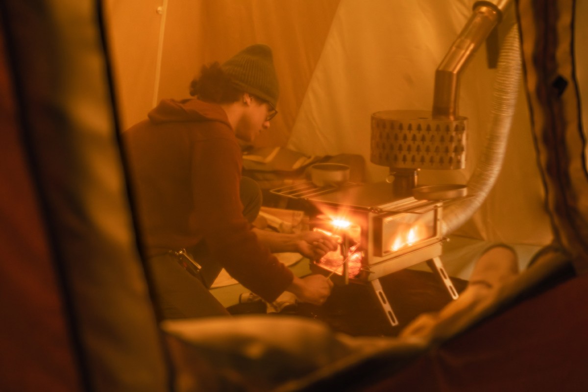 A person tends a wood stove inside the Springbar Skyliner hot tent