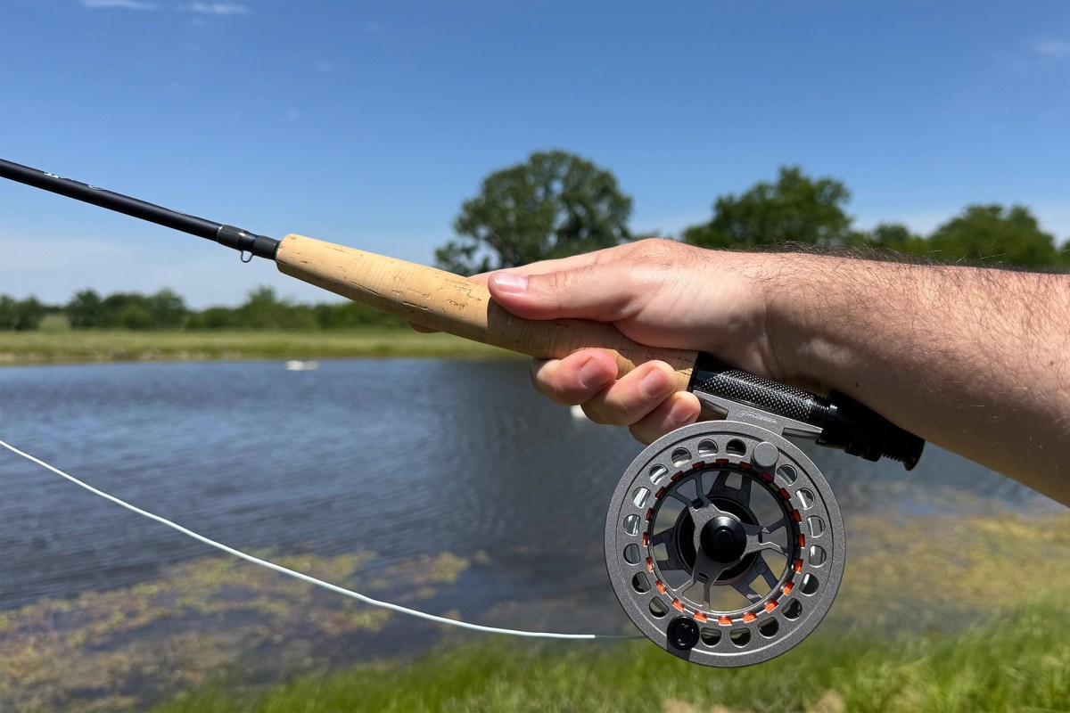 Hand holding the fly rod and reel with line out beside a pond
