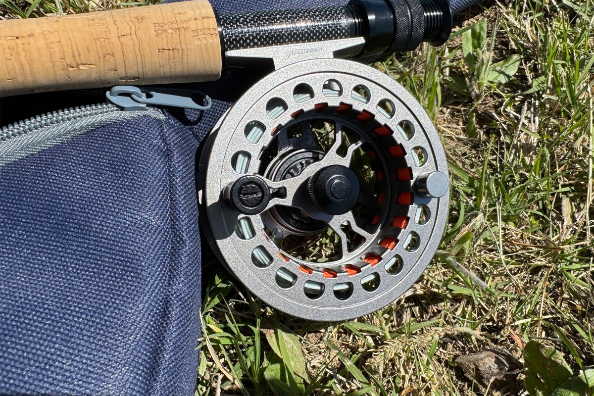 Close view of the fly reel, cork handle, and rod case in the grass