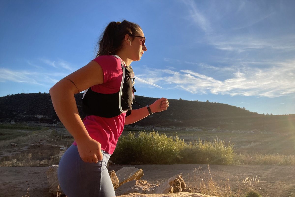 Running Vests Should fit Snuggly, Without any Bounce A woman runs in the sunset with a hydration pack