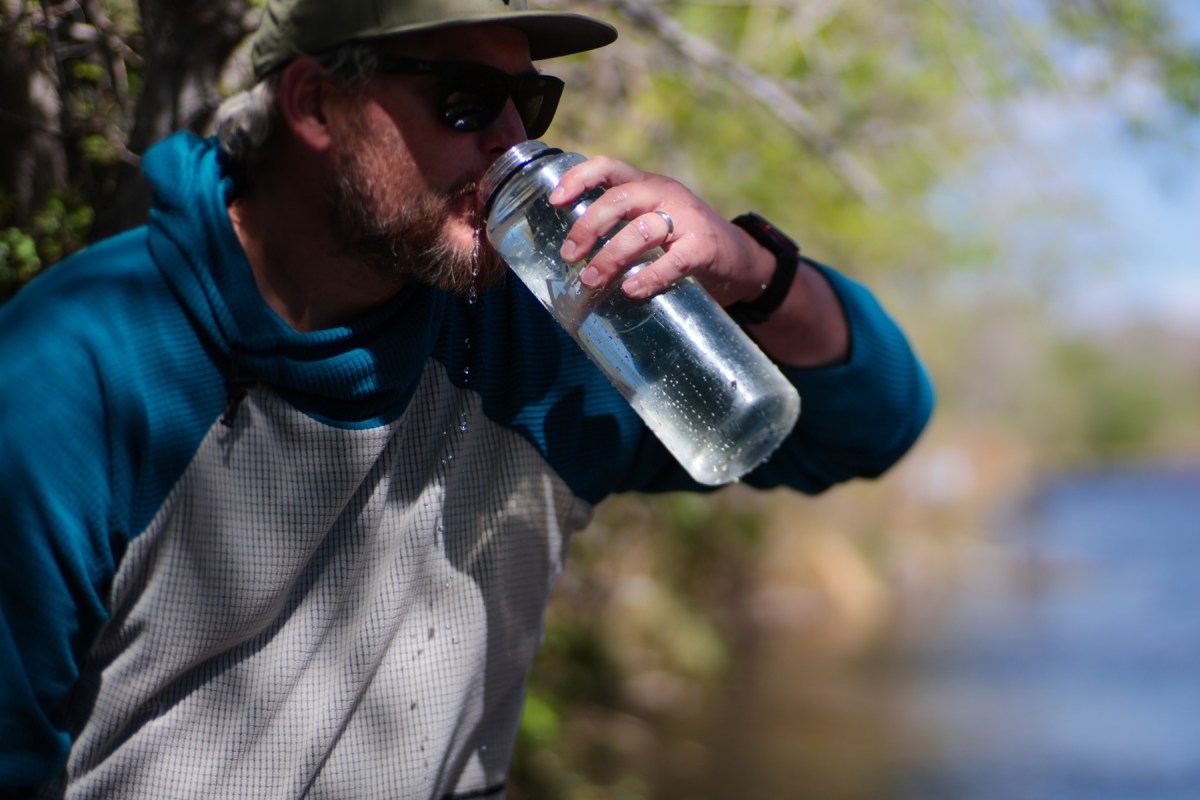 Person drinking from a clear bottle after filtering water near the lake