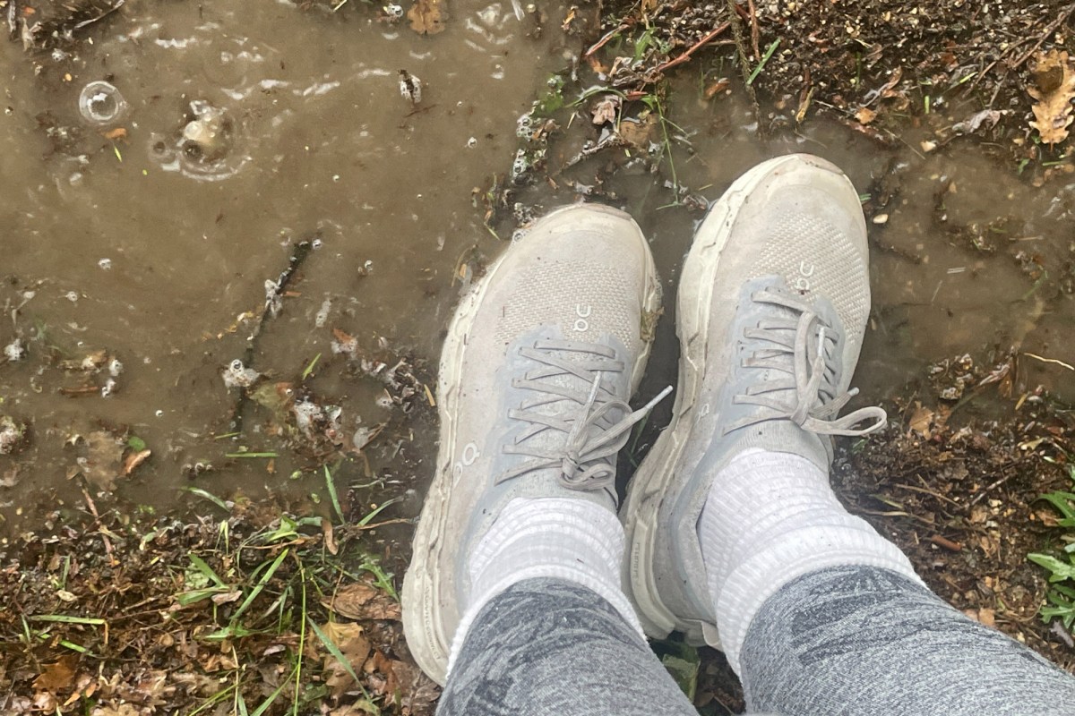 On Cloudsoma trail runner stepping through muddy water on a wet trail