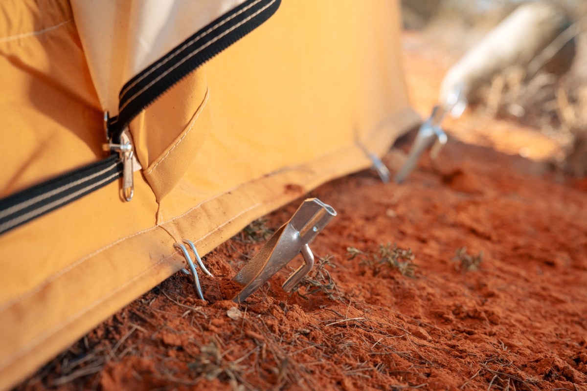 Metal tent stakes secure the canvas tent edge in red dirt