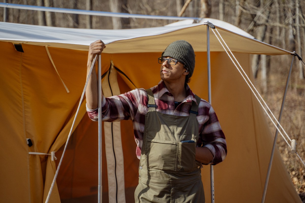 A person adjusts the awning pole and guyline on a canvas tent