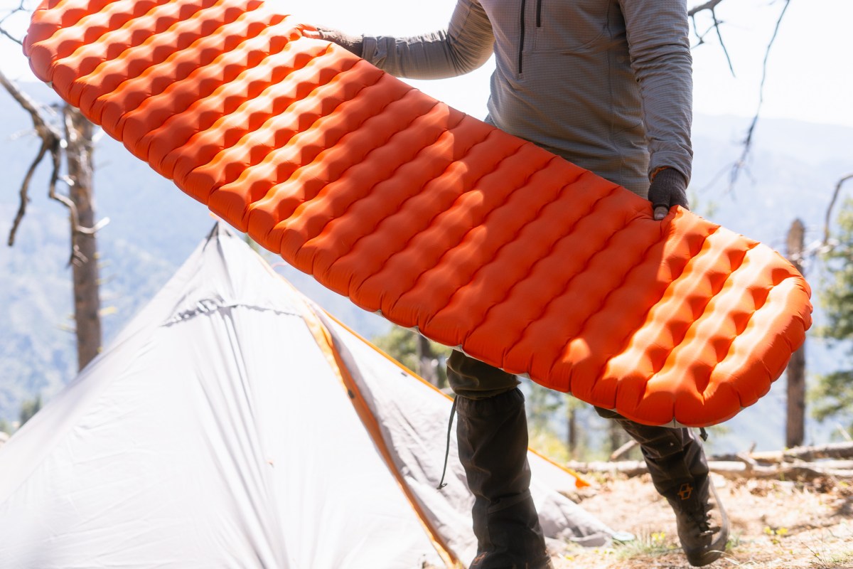 Orange side of the NEMO Tensor sleeping pad held beside a tent at camp