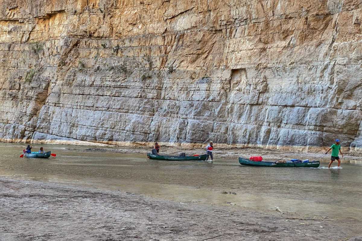 people walk/paddle canoes through river