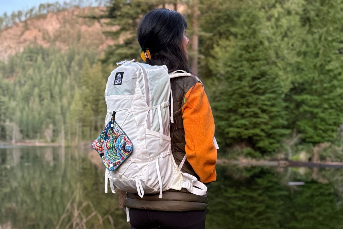 rear view of women standing by lake wearing daypack