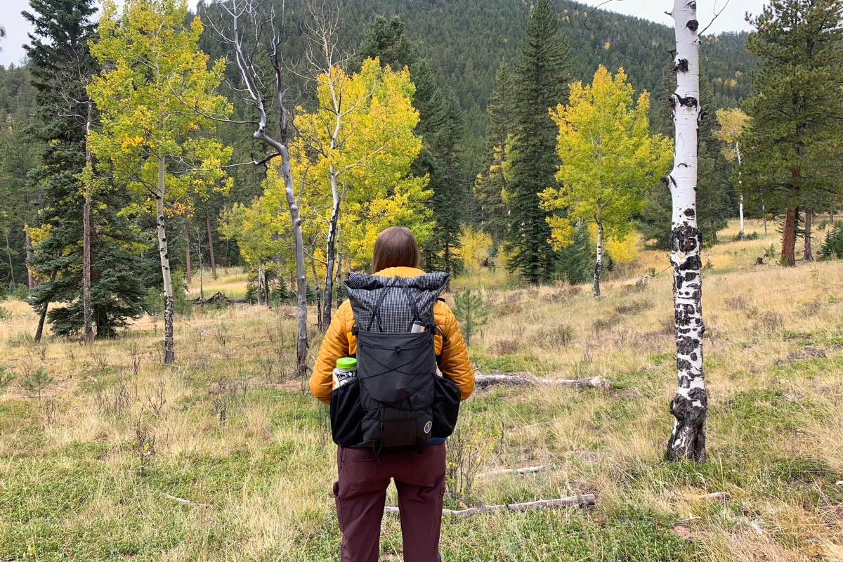 a hiker in a yellow puffy jacket hiking with the symbiosis pack amongst aspen trees