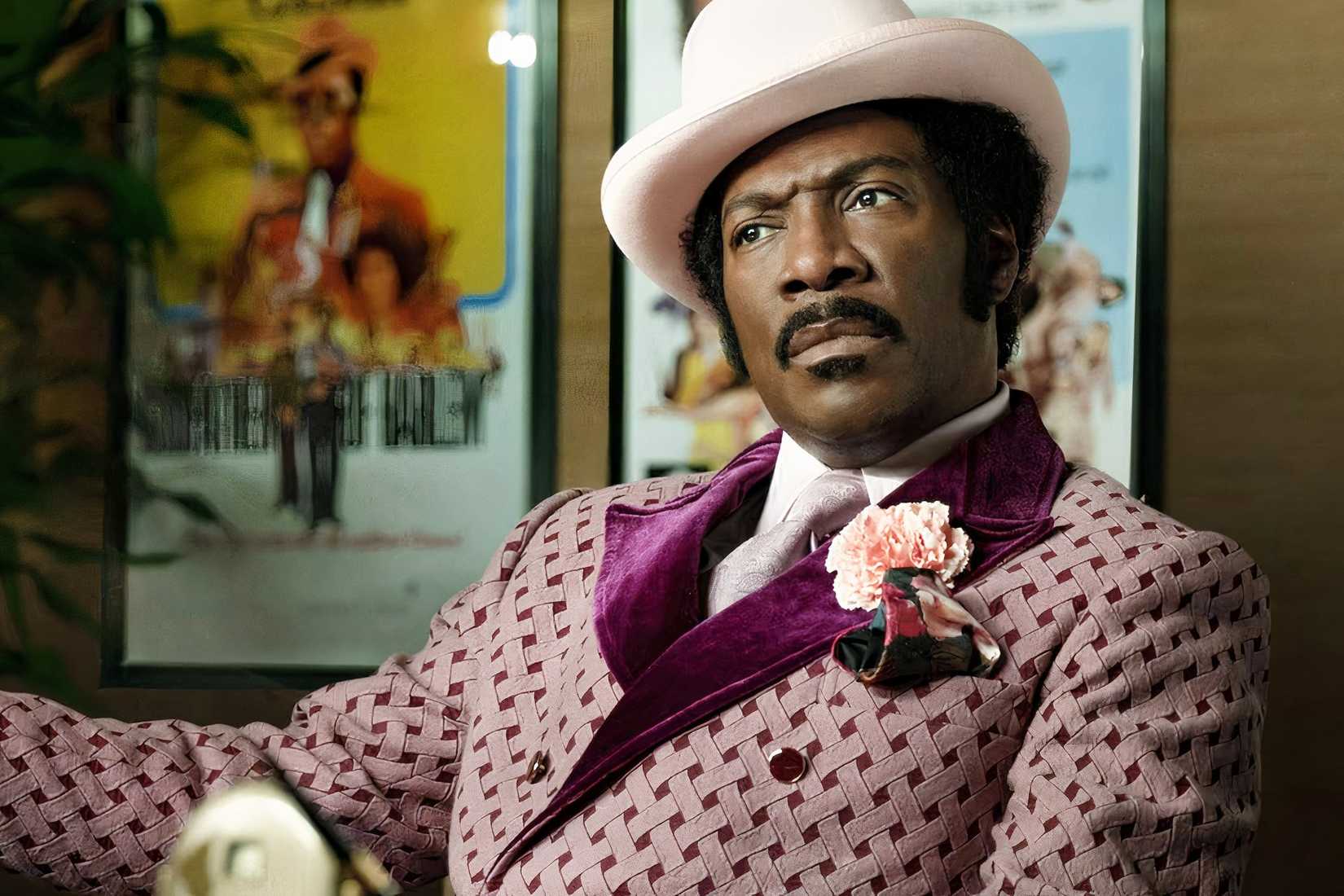 Rudy Ray Moore sits in a pink suit and white hat in Dolemite Is My Name.