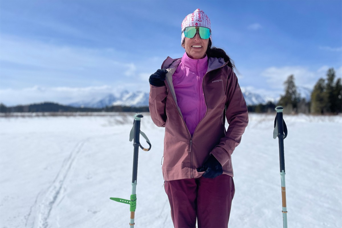Woman wearing a Delta Jacket under a shell while standing on a snowy ski trail