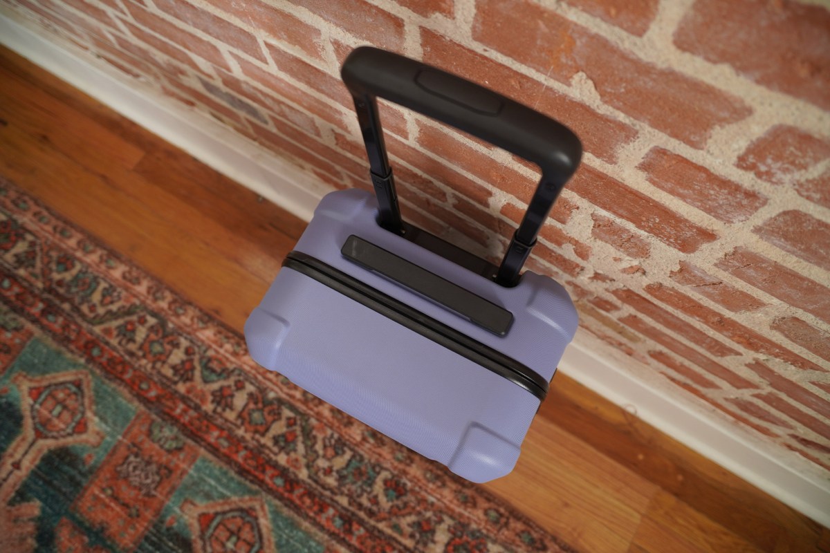Top view of the Cotopaxi carry on luggage with the telescoping handle extended next to a brick wall